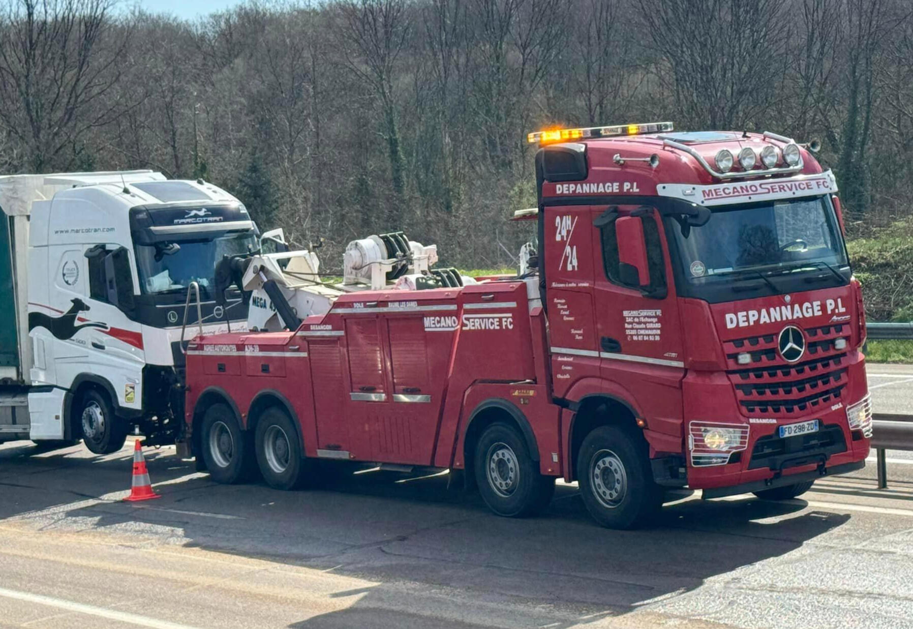 Remorquage Poids Lourd | Camion remorqueur 60T Mecano Service FC sur autoroute A36 Imposant camion remorqueur rouge Mercedes de Mecano Service FC intervenant sur un poids lourd Renault blanc en panne sur l'aire d'autoroute A36 près de Besançon. Le dépanneur PL 8x4 avec ses gyrophares allumés est équipé d'un puissant système de levage pou