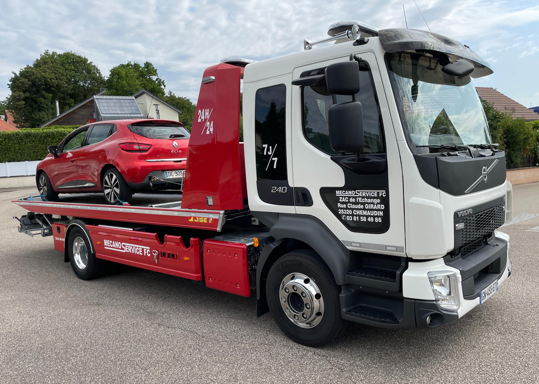 Dépannage Renault Clio | Transport sécurisé par dépanneuse Volvo Mecano Service FC 24h/24 Besançon Dépanneuse Volvo blanche et rouge de Mecano Service FC transportant une Renault Clio rouge sur son plateau. Le véhicule de remorquage moderne est stationné dans une zone résidentielle de Besançon, avec les coordonnées de l'entreprise visibles sur la porti